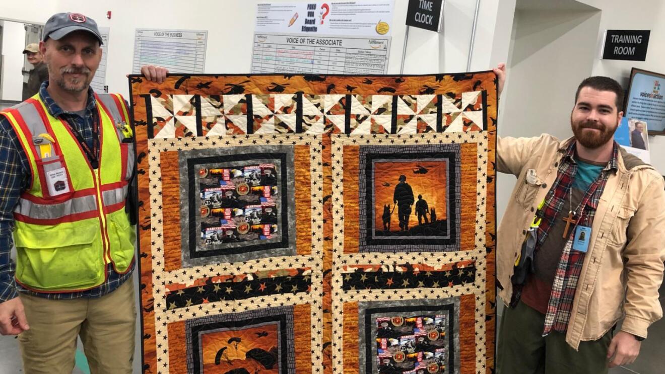 Amazon associate holds up a custom quilt with his General Manager, whom the quilt was gifted to.