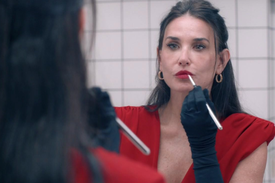A woman putting lipstick on from the Oscar-nominated movie, The Substance.