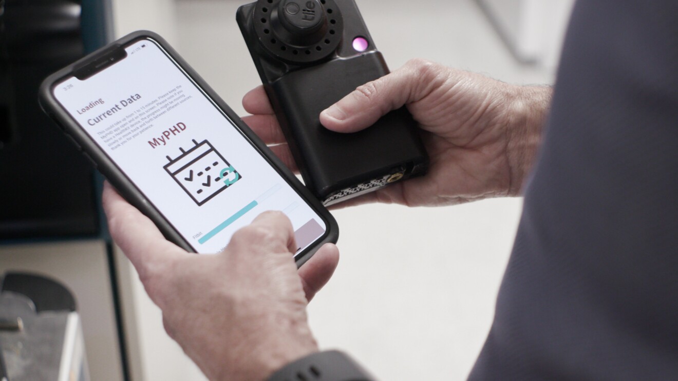 Michael Snyder, PhD, professor and chair of genetics for Stanford University’s School of Medicine holds his smartphone showing the results of tested diagnostics. In his other hand he holds a black testing device.