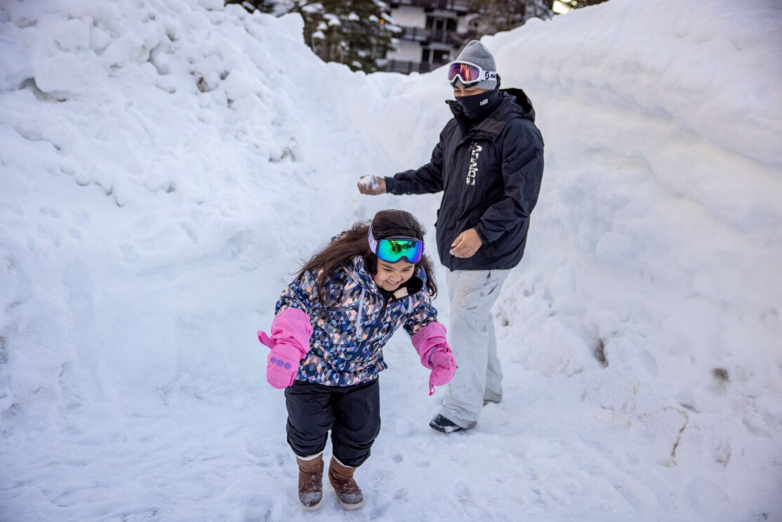 A dad and his daughter play in the winter snow.