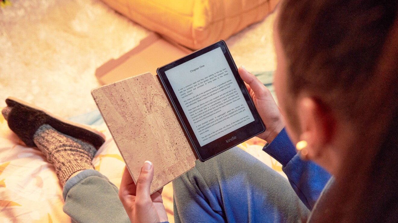 A woman holds a kindle e-reader while reading a book on the screen