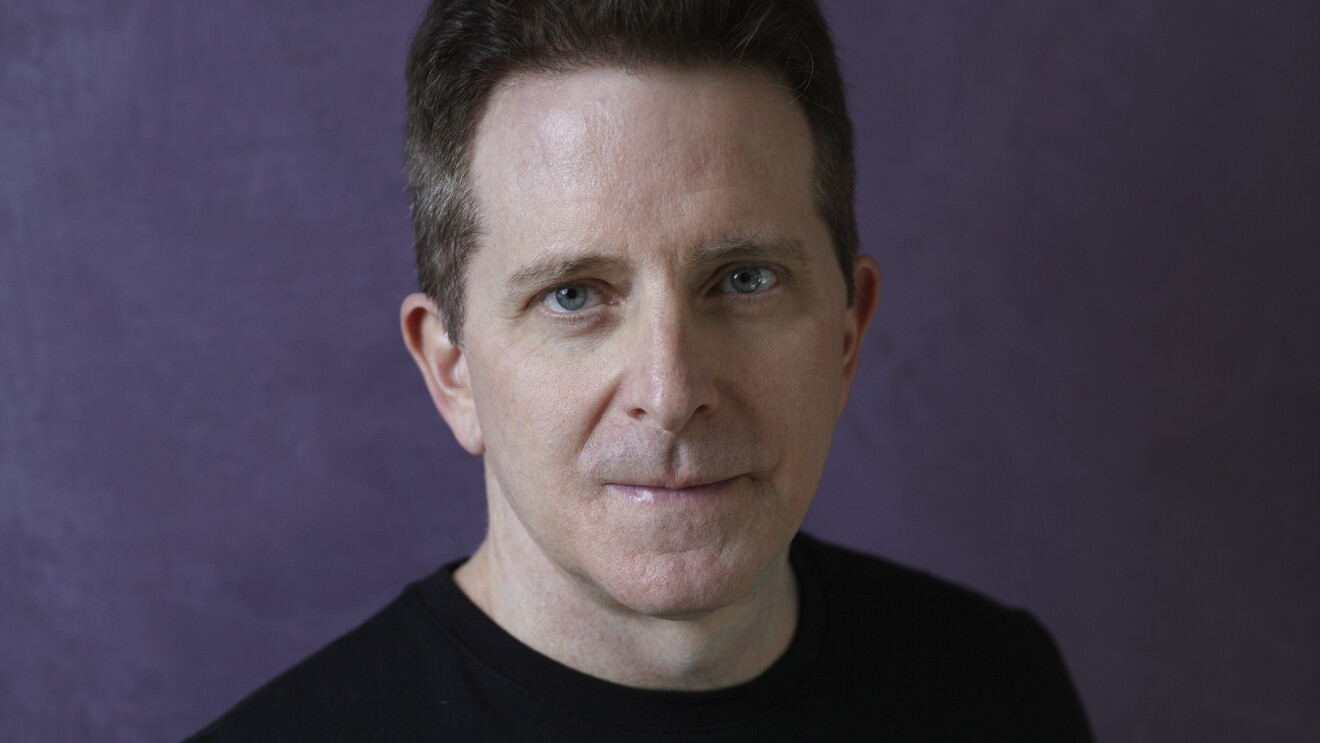 Amazon author Landon J. Napoleon stares into the camera. He has dark hair, blue eyes, and is wearing a black sweater. The background is purple. 