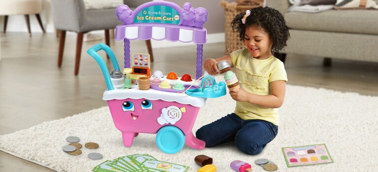 An image of a child playing with a toy ice cream stand in her living room.