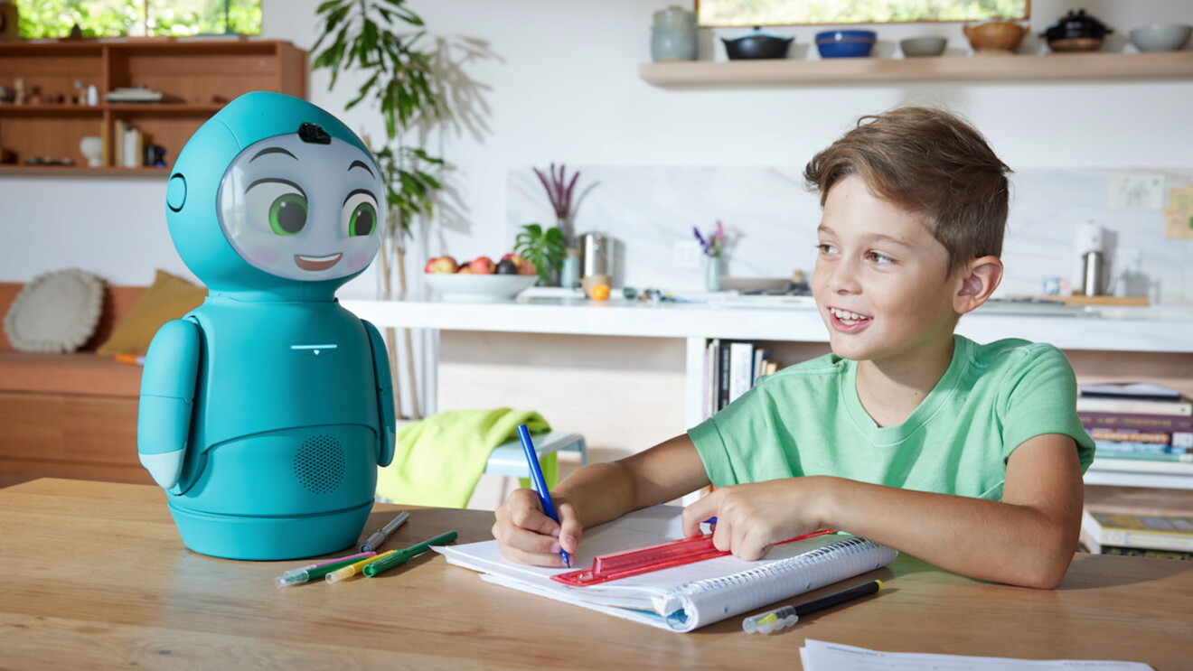 Una imagen de un niño interactuando con Moxie y escribiendo en un cuaderno.
