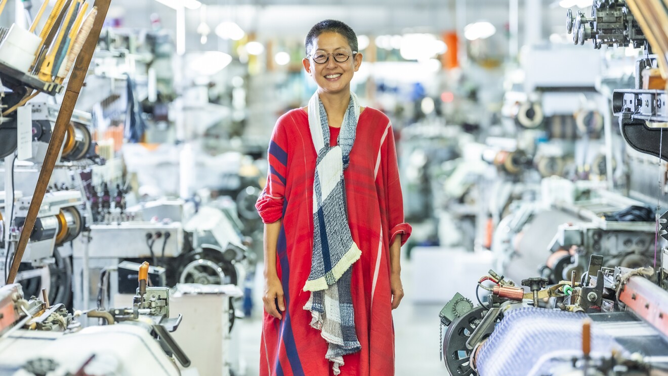 織機の前に立つ赤いワンピースを着てメガネをかけた女性