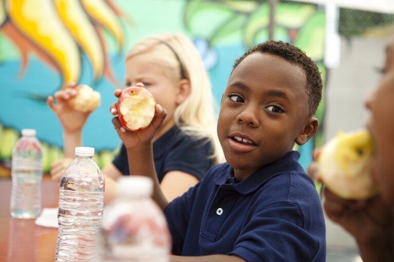 As part of No Kid Hungry, kids in a school setting eat their apples.