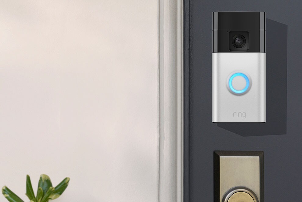 Ringドアベルの本体カラーシルバーが玄関ドアの鍵穴上部に設置され、正面のLEDリングが青く点灯している。