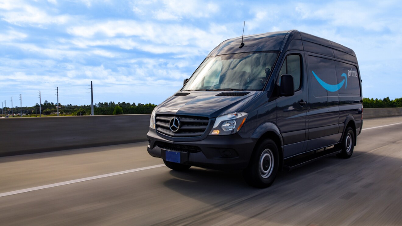 A cargo van decorated with the Amazon smile logo and the word "Prime" drives down the road.