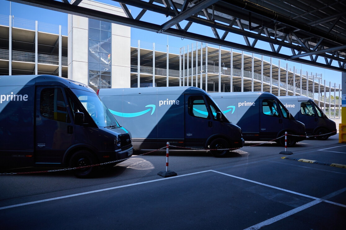 Neue Amazon Rivians nebeneinander aufgereiht vor einem Parkhaus.