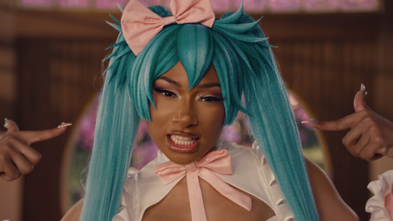 A close-up image of Megan Thee Stallion dressed in a blue wig with pigtails and a pink bow. 