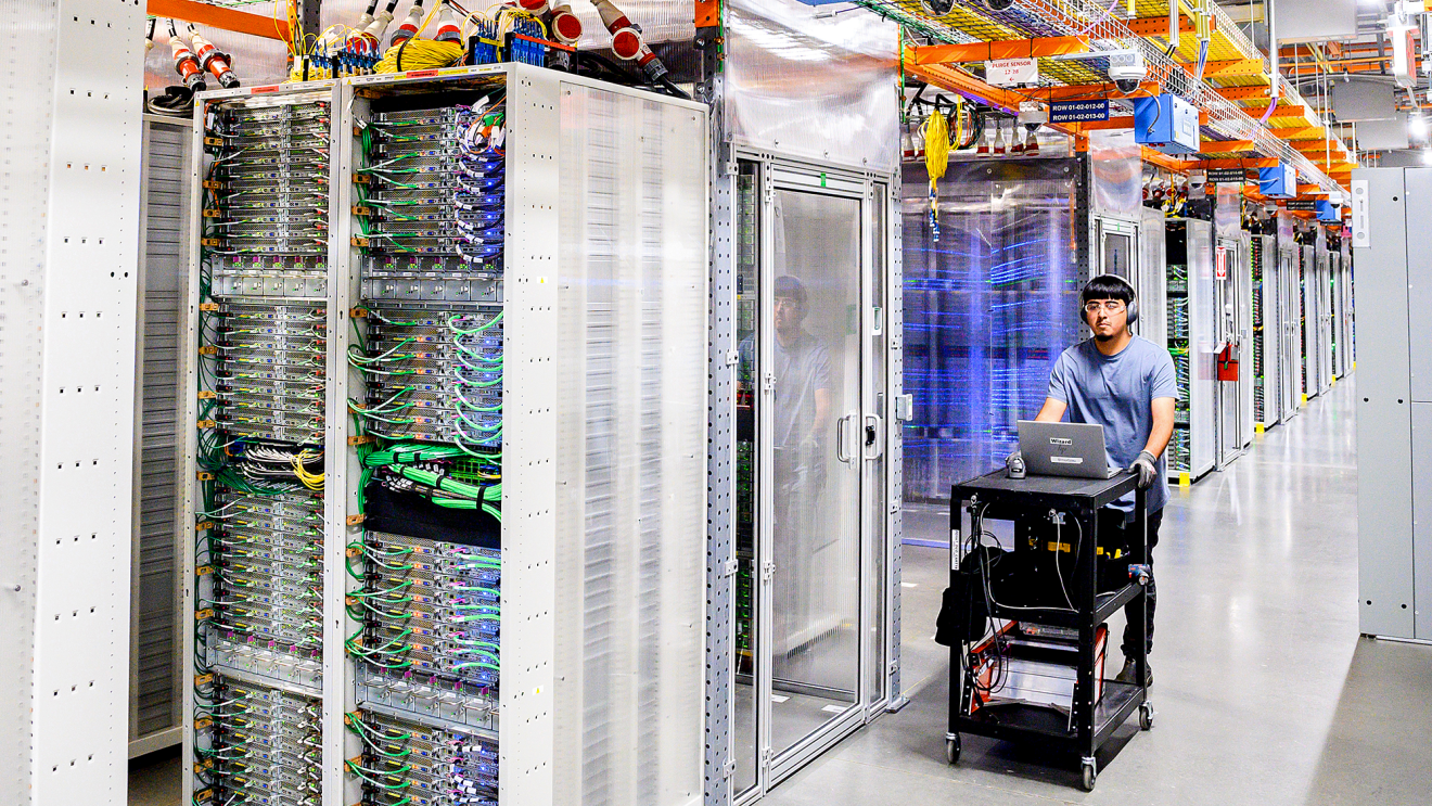 A technician pushing a cart that holds their laptop through servers inside a data center.