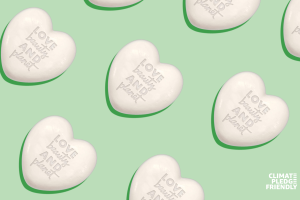 A light green color as the background with the Climate Pledge Friendly logo in white font placed in the bottom right corner. White solid 3D hearts that read "love beauty and planet" are placed diagonally across the image.