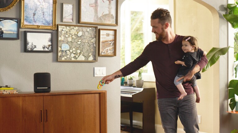 A man holds a baby in their home. He sets down the baby's toy on a console where an Alexa device sits.