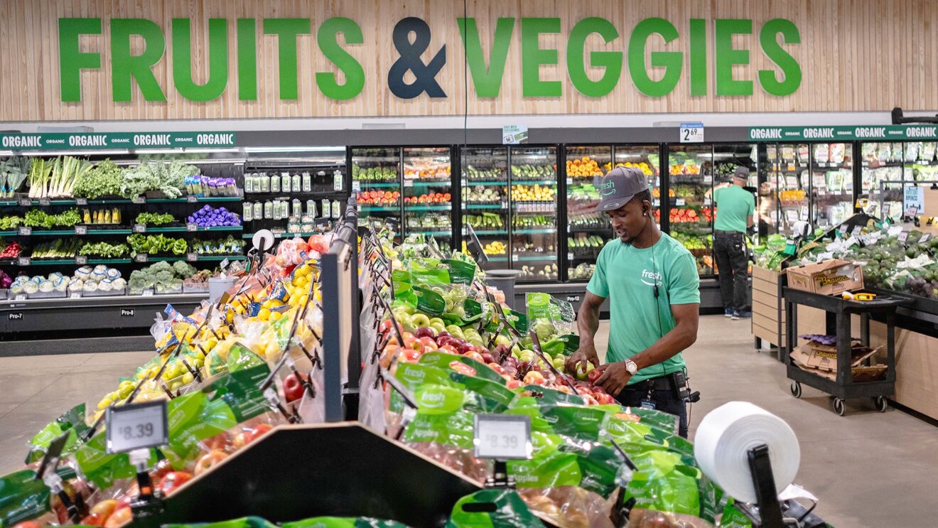 A photo of an Amazon Fresh employee placing apples on a Amazon Fresh store shelf.