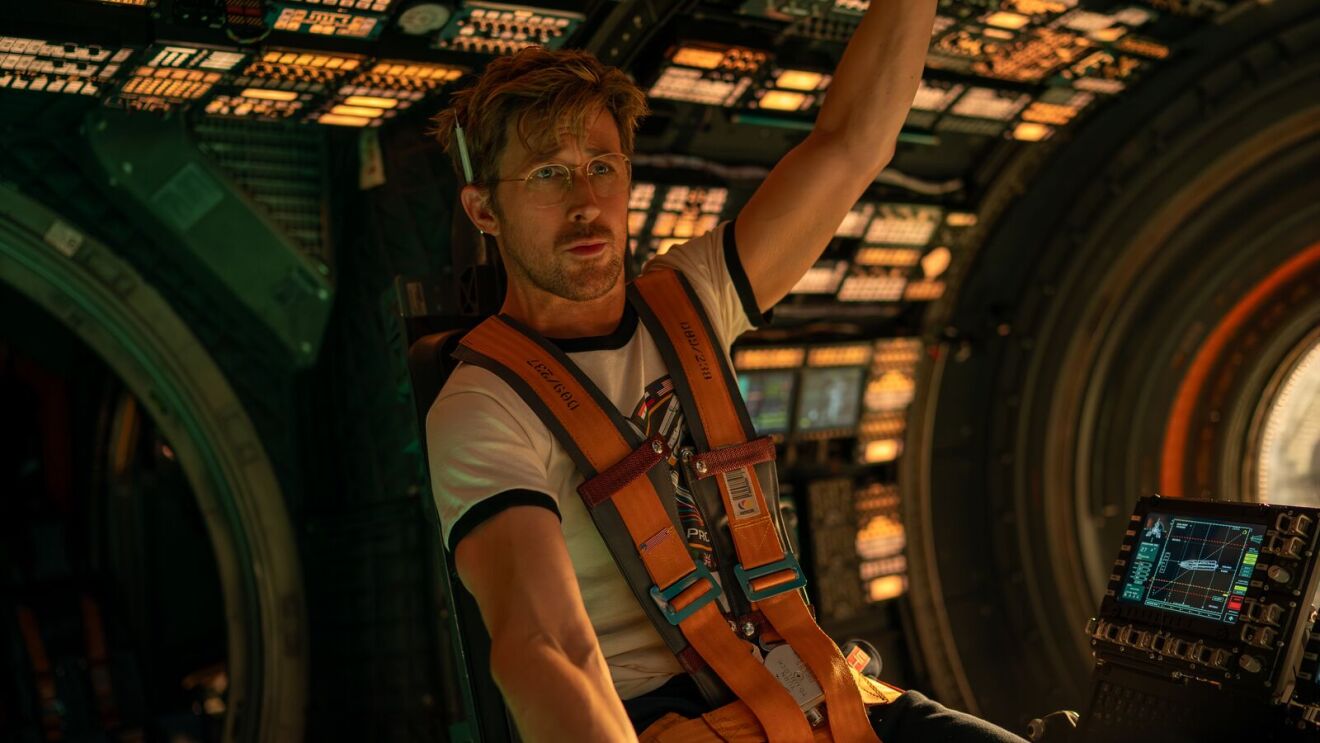 A scene from Project Hail Mary starring Ryan Gosling as Ryland Grace in white shirt with orange harness inside spacecraft