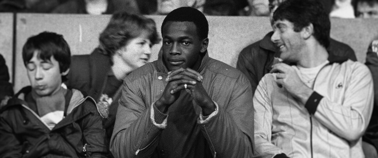 Schwarz-Weiß-Bild mit Justin Fashanu als Zuschauer bei einem Fußballspiel. Sein Schicksal erzählt die neue Prime Video-Doku: DAS LETZTE TABU.
