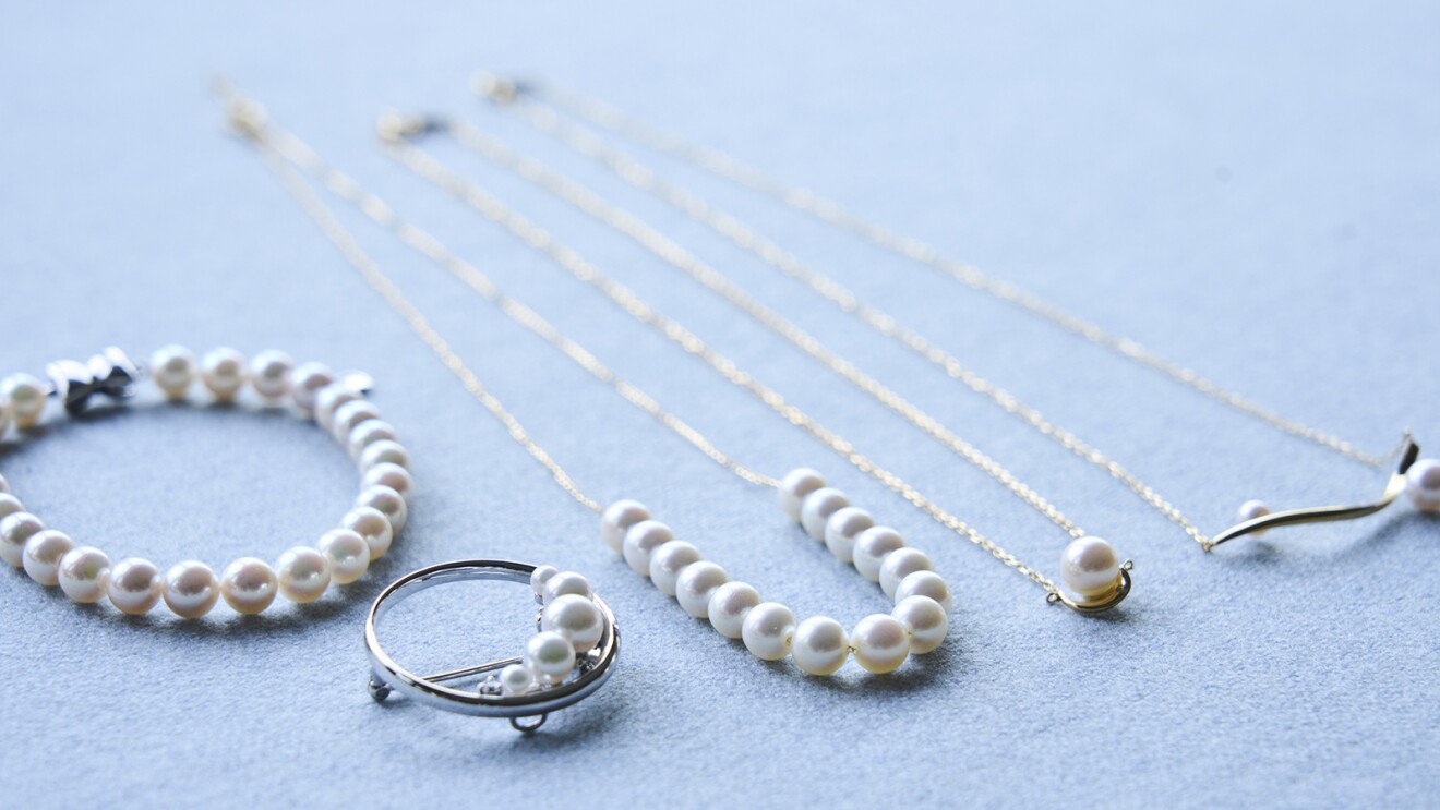 薄いブルーの布の上に置かれた真珠のブレスレット、ブローチ、ネックレス、ペンダント