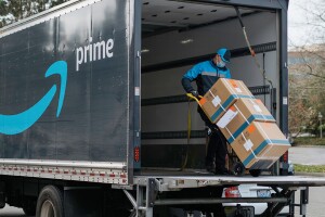 An Amazon DSP partner loads three boxes on a trolley into an Amazon delivery truck.