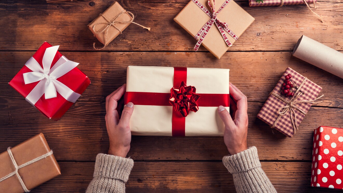 A flatlay of a pair of hands holding a wrapped gift, with other wrapped gifts scattered around the table.