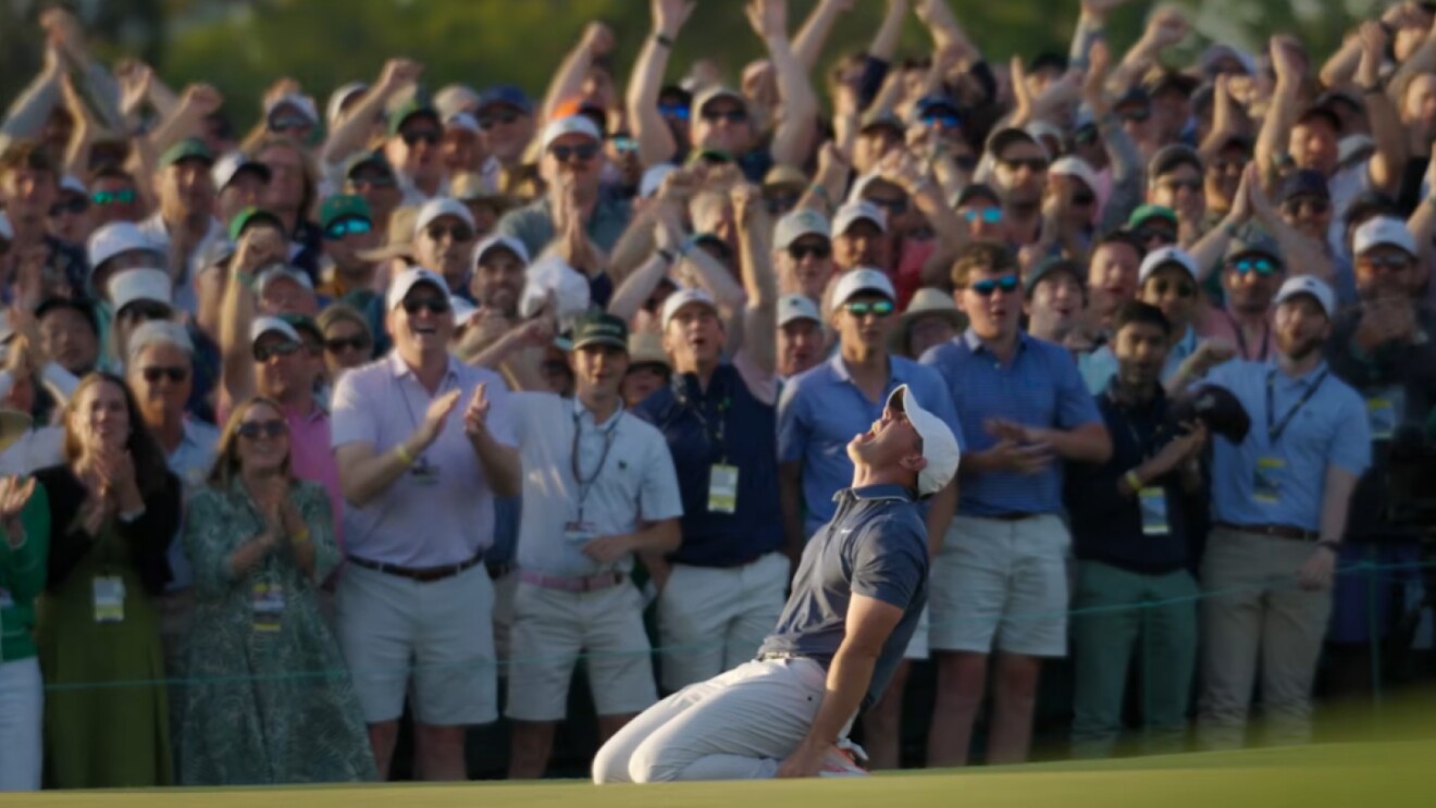 Rory McIlroy on his knees celebrating after winning the 2025 Masters, with the crowd in the background.