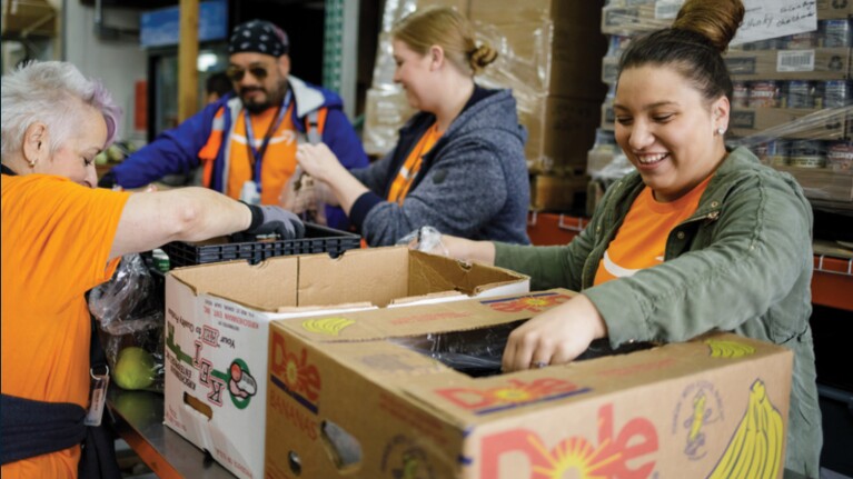 A photo of four Amazon employees preparing boxes of food items for donation in a fulfillment center.