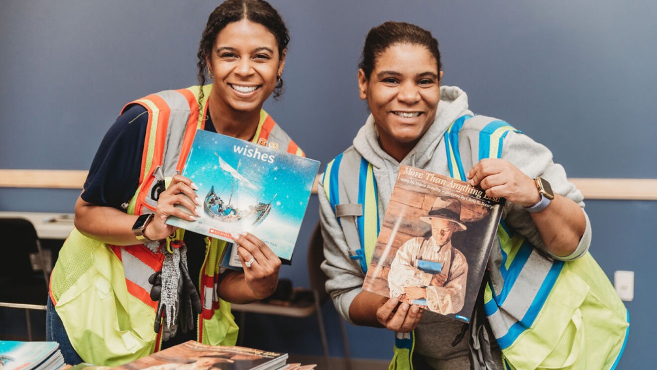 An image of two women holding books and smiling wearing neon vests.