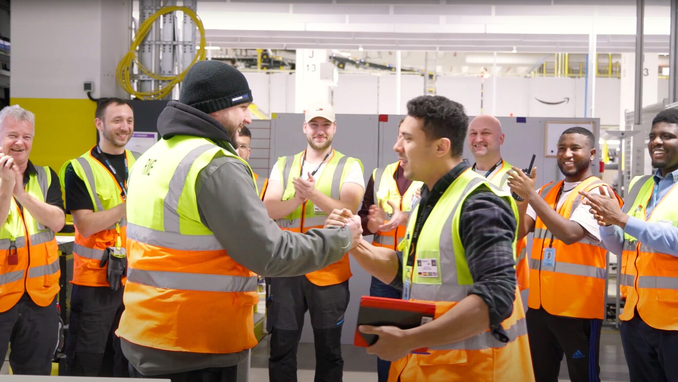 Dennis mit Kolleginnen und Kollegen an seinem Arbeitsort, dem Amazon Logistikzentrum in Oelde.