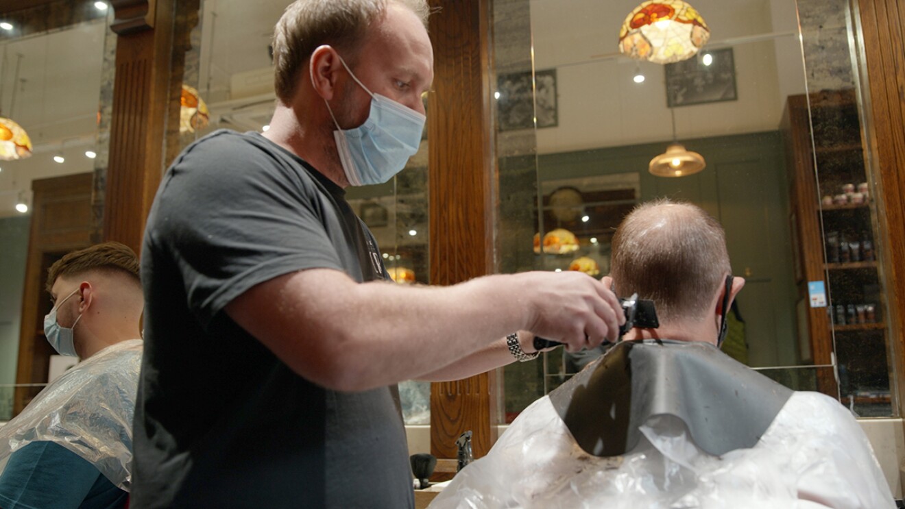 An image of a man wearing a mask while cutting another man's hair.