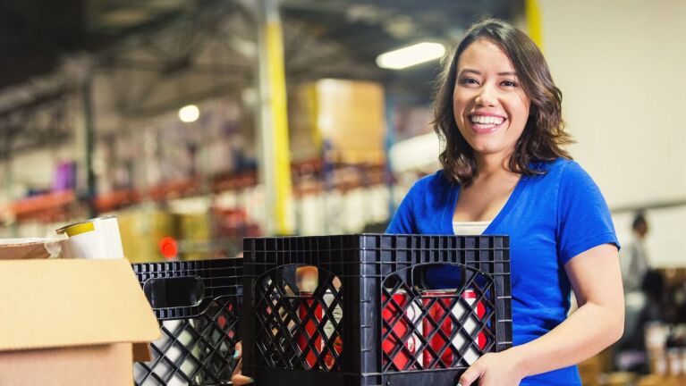 Woman smiling in blue shirt holding plastic crates in warehouse