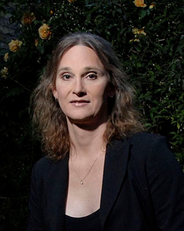 A headshot photo of Jessica Bussert smiling for a photo in front of a wall with greenery and yellow roses on it. 