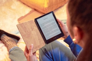 A woman holds a kindle e-reader while reading a book on the screen