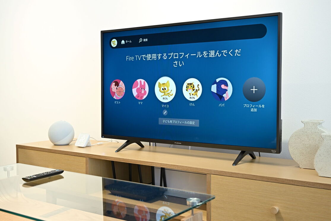 木製のテレビ台の上に置かれた黒いテレビ。その画面に５つの円があり、その中にイラストのキャラクターが書かれている、それぞれの下にパパなどの文字が見える