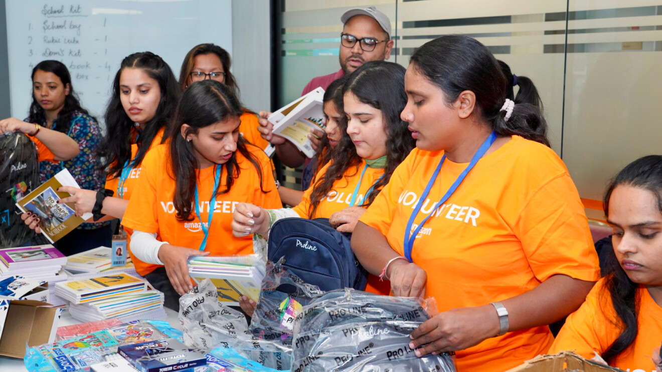 Amazon volunteers in orange t shirts fill backpacks with emergency supplies