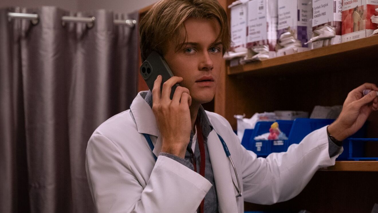 Conrad Fisher (Christopher Briney) dressed in medical clothing on phone while in supply closet