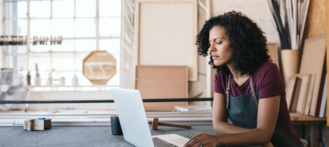 A woman entrepreneur sits at a workbench, while working on her computer.