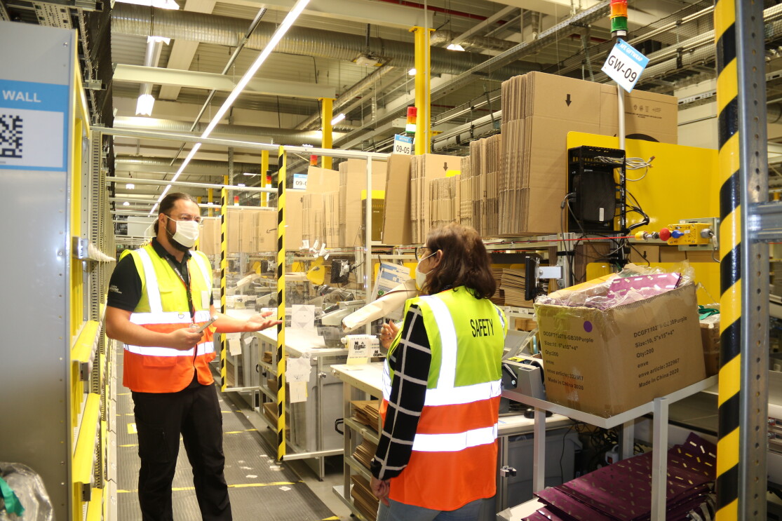 Amazon-Arbeitssicherheitsexperte Lucian Geiger mit Kollegin in gelb-orangenen Westen im Logistikzentrum.