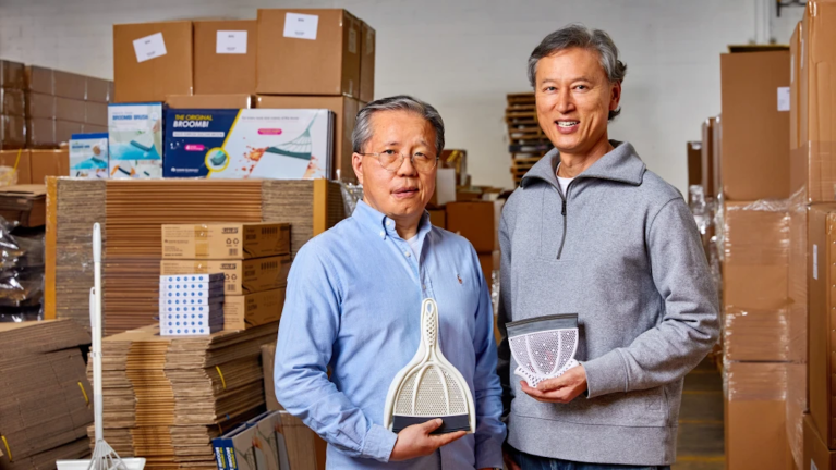 People standing in a product stockroom holding Broombi bristleless brooms with shipping boxes and inventory on shelves behind them.