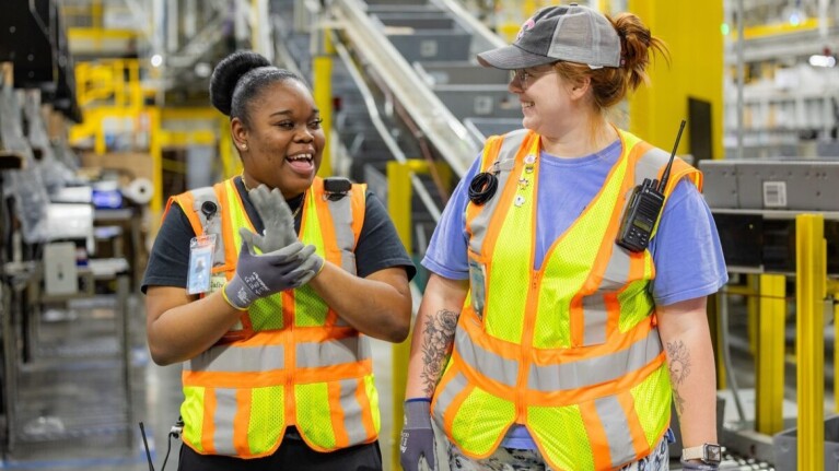 Women in safety vests laughing together in a warehouse