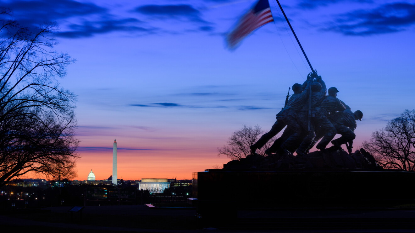 US Marine Corps War Memorial in front of a sunset with the Lincoln Memorial, Washington Monument, and US Capitol dome receding toward the horizon