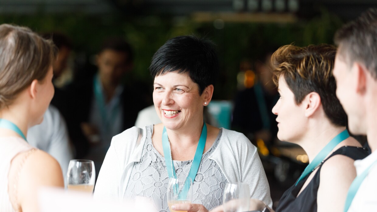 Tre donne e un uomo con portabadge azzurri conversano reggendo bicchieri