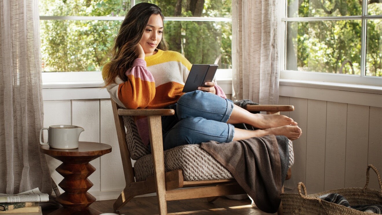 Una mujer descansa en una silla, con los pies hacia un lado, leyendo un nuevo Kindle Paperwhite de Amazon.