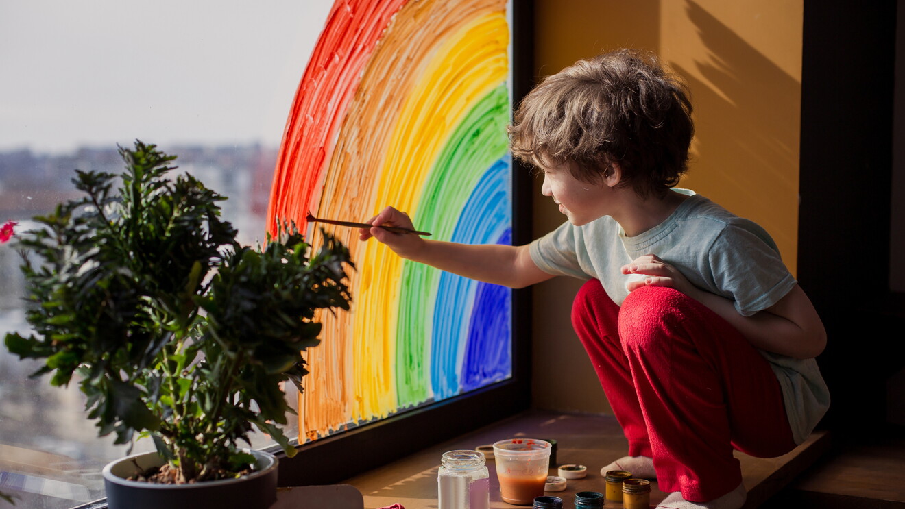 A child placing homemade rainbows in the window of their home, during COVID-19 pandemic.