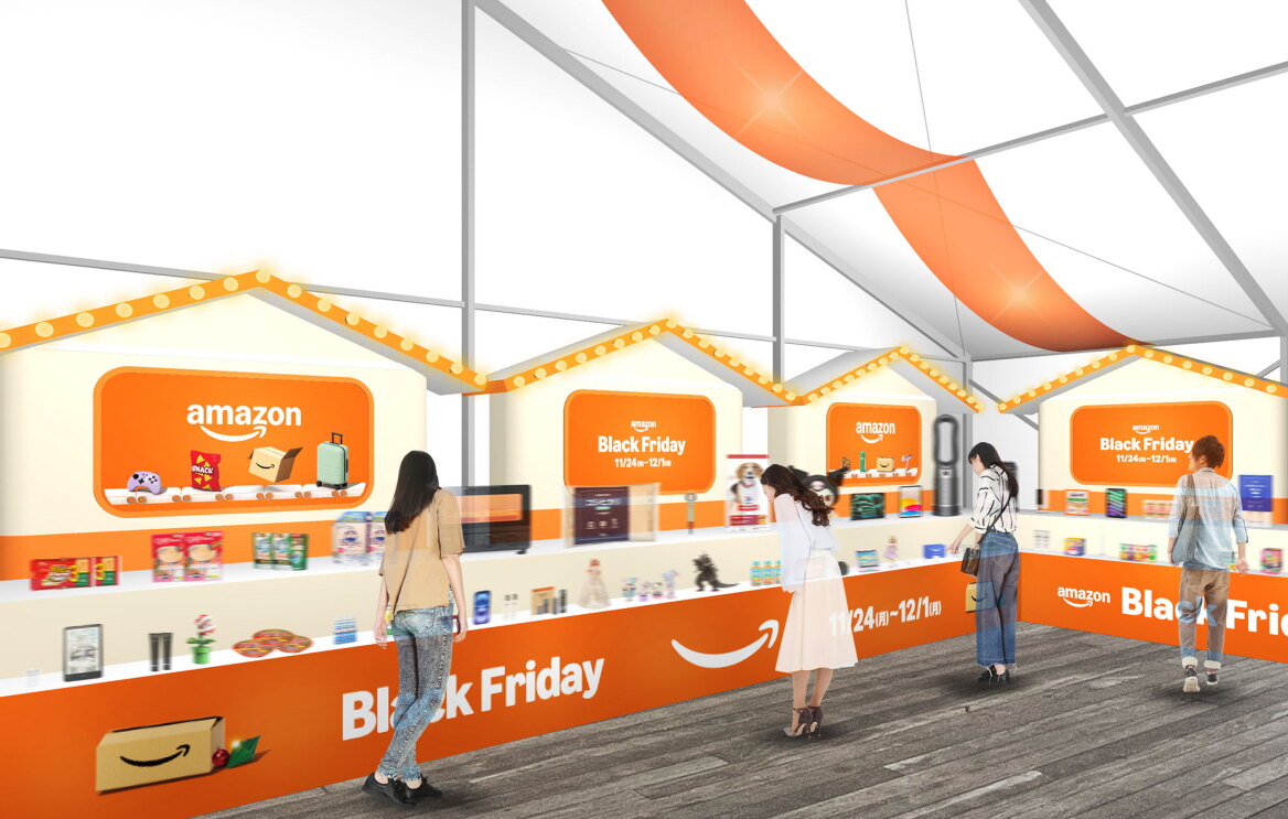 白い仮設テント内部各所にオレンジ装飾。Amazonのロゴと「Black Friday」の文字入りのオレンジのパネルやボードで飾られた陳列台に、さまざまな商品を展示。人々が商品を見て回る。