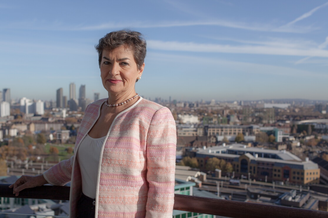 Christiana Figueres standing on a balcony overlooking a city skyline.