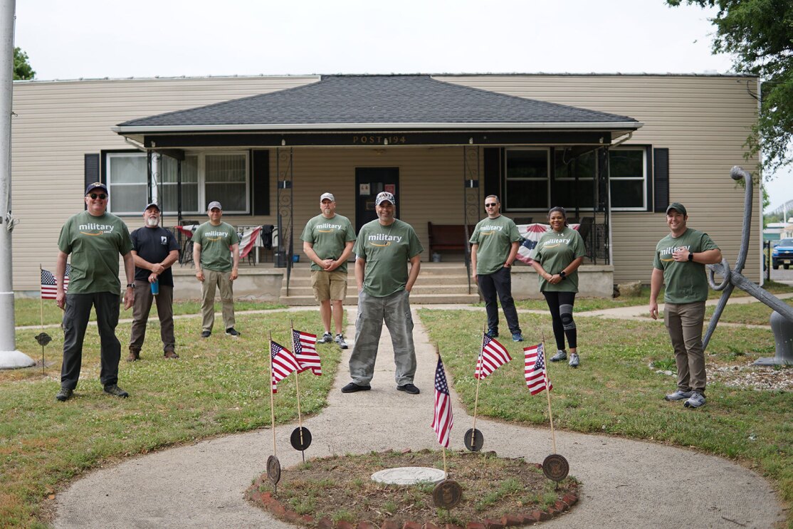 Warriors@ members stand for a photo in a yard outside of a building. There are flags in front of them.