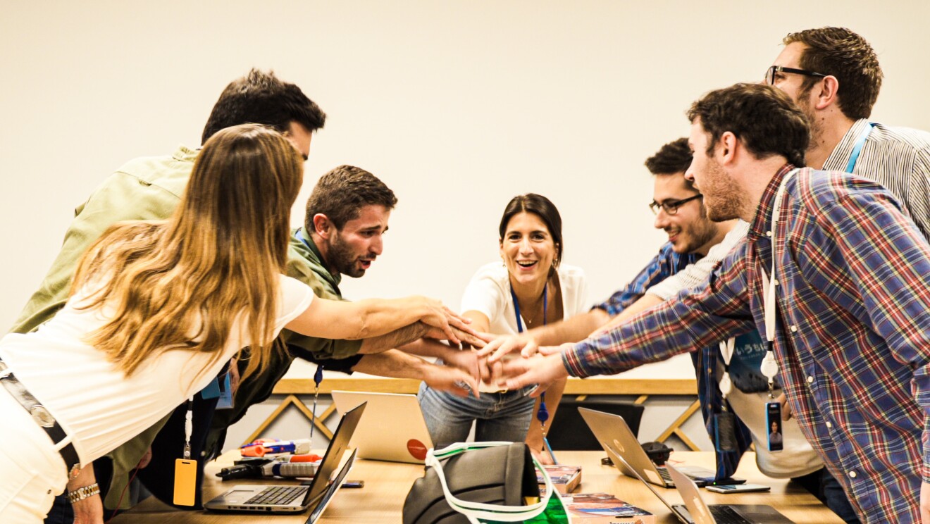 El equipo que ha estado preparando Prime Day se encuenta en la war room  celebrando el inicio de un intenso día. Siete jóvenes amazonians juntan las manos en el centro de la mesa. Una mesa que está llena de ordenadores y cajas de pizzas.  