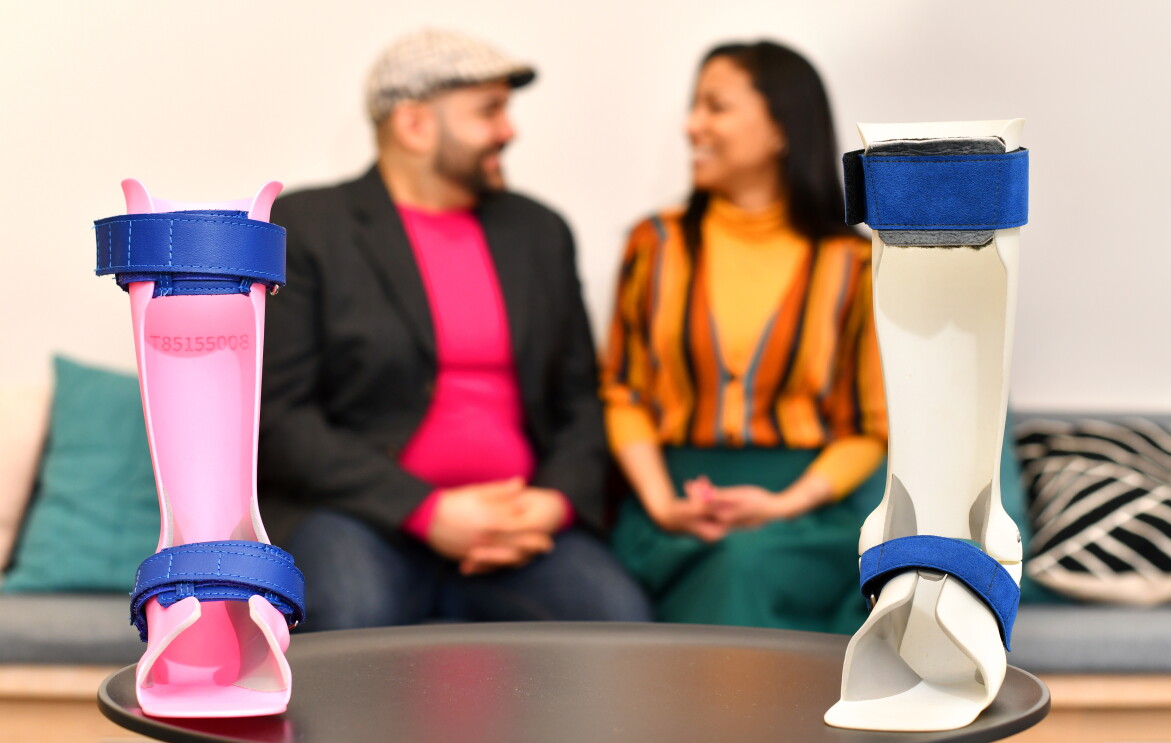 In the forefront, two ankle orthoses for children produced by Andiamo, a smaller one in bright pink plastic and a bigger one in white plastic with blue straps. In the background, Samiya and Naveed Parvez smile at each other.