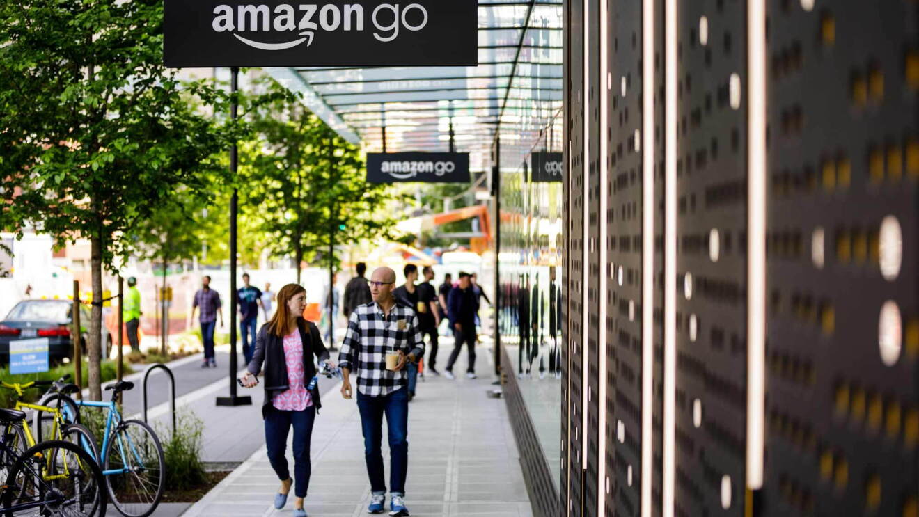 Amazon employees walk on the sidewalk past Amazon Go flagship store in Seattle, Washington
