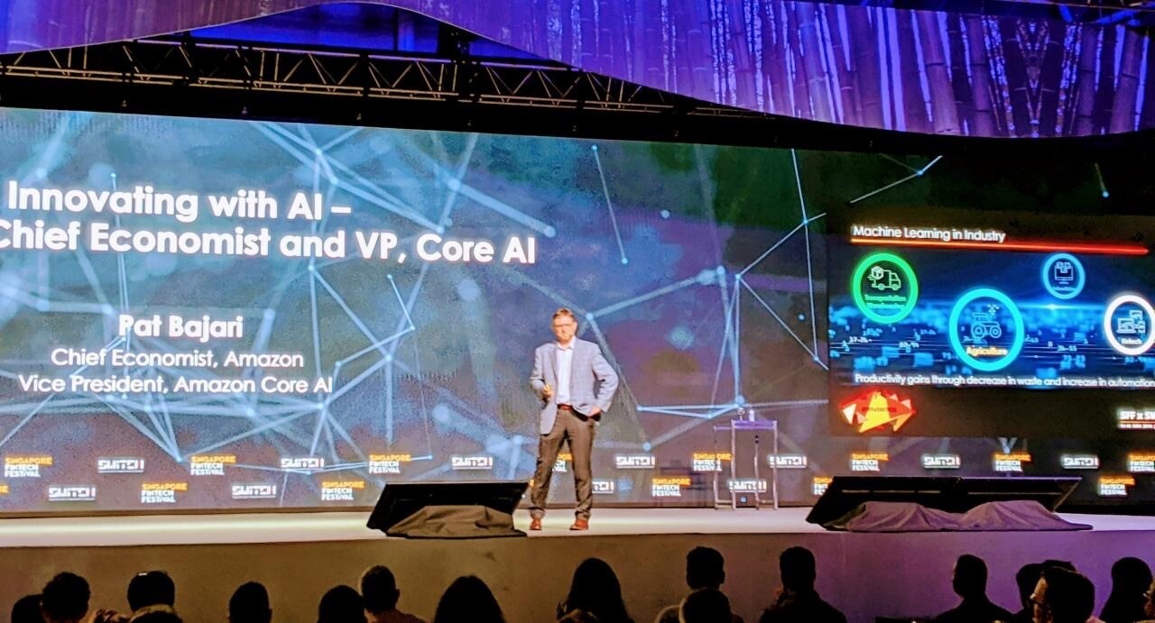 A man stands on stage at a conference, presenting on "Innovating with AI"