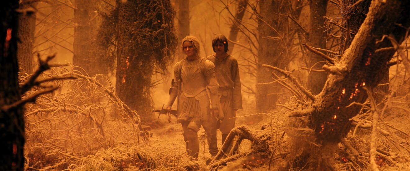 Morfydd Clark (Galadriel), Tyroe Muhafidin (Theo)  navigating charred landscape from raging bushfire in Lord of the Rings: The Rings of Power